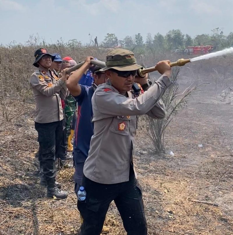 Keterangan Foto: Kapolres Way Kanan AKBP Ramadhona, S.H., S.I.K., saat melakukan penyemprotan air di lokasi titik api kebakaran hutan dan lahan.