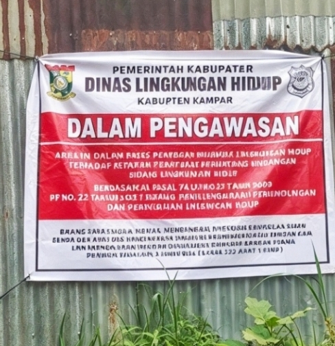 Keterangan Foto: Gudang berpagar seng yang dipasangi banner bertuliskan “DALAM PENGAWASAN” oleh DLH Kabupaten Kampar. Lokasi tersebut diduga menjadi tempat pengolahan oli bekas atau oli oplosan. (dok.ist) 