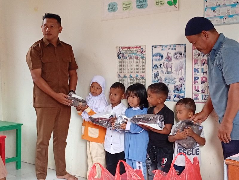 Ket. Foto : Pj Geuchik Andi Iskandar Rizza melalui Sekretaris Desa (Sekdes) Sarizal dan Ketua Tuha Peut Gampong Tgk.Mustafa menyerahkan Baju Seragam Polisi kepada Anak PAUD Bunda Cinta Raja (09/09/2025) 